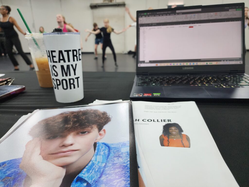 musical theatre audition room, computer and headshot on table with dancers in the background